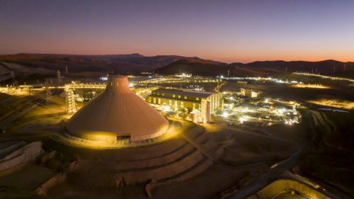Lit industrial complex at dusk with mountains in the background.